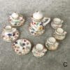 Miniature floral teapot set with cups and saucers, placed on a gray surface, decorated with colorful flower patterns.