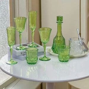 Green glassware set with various drinkware pieces and a carafe on a white table near a window.