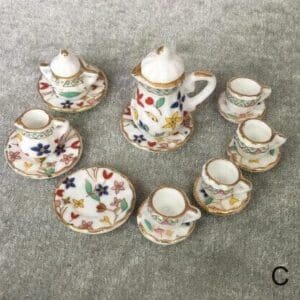 Miniature floral teapot set with cups and saucers, placed on a gray surface, decorated with colorful flower patterns.
