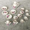 Miniature porcelain tea set with floral designs on a gray surface, including plates, cups, and teapots.