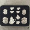 Miniature black and white floral tea set with plates, cups, and teapot arranged in a foam tray.