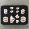 Miniature tea set with floral designs on a black tray, including cups, saucers, a teapot, and a creamer.