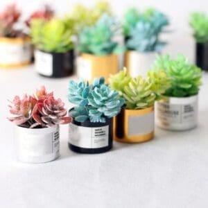 Colorful artificial succulents in small decorative pots arranged on a light surface.