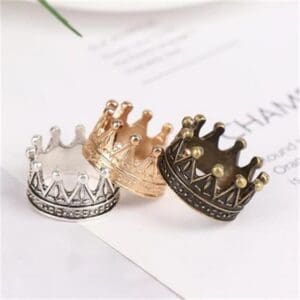 Three crown-shaped rings in silver, gold, and bronze, displayed on a white paper background.