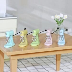 Five pastel-colored toy stand mixers with heart whisks arranged on a wooden table.