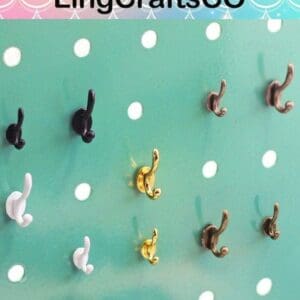 Various small hooks in black, white, gold, and bronze are displayed on a green pegboard with circular holes.