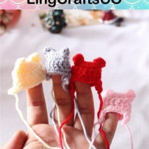 Four crocheted mini hats on fingers, in yellow, gray, red, and pink. Background shows a blurred festive scene.