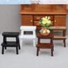 Miniature stools in black, white, and wood finish with a vase of yellow roses, set against a wooden cabinet.