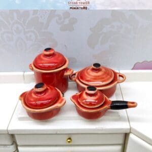 Set of four red miniature kitchen pots with lids on a white countertop.
