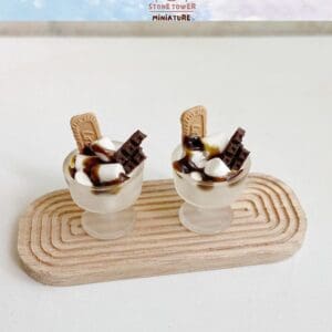 Two miniature dessert cups with chocolate, cookies, and marshmallows on a wooden tray.