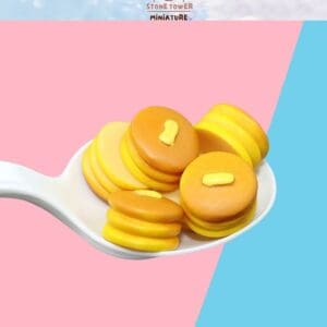 Miniature pancakes with butter on a spoon, set against a pink and blue background.