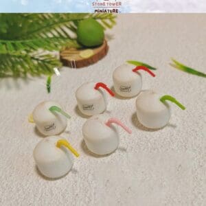 Miniature coconuts with colorful straws on textured surface, surrounded by green leaves and sliced lime decoration.