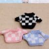 Three miniature checkered sweaters in black, pink, and blue on a beige background.