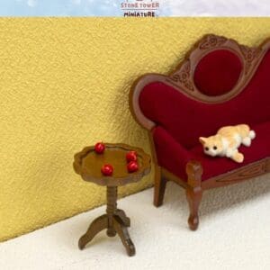 Miniature scene with a brown table holding red berries, a red and brown sofa, and a small cat figure on the sofa.