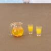 Miniature pitcher with orange liquid and two matching shot glasses on a brown surface.
