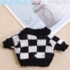 Black and white checkered knit sweater on a textured beige surface beside a magazine with a jar image.