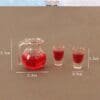 Miniature clear pitcher and two shot glasses with red liquid, showing dimensions: pitcher 2.1x2.3cm, glasses 1.5x0.9cm.