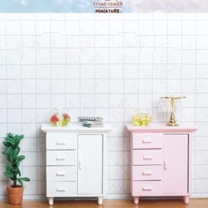 Two miniature cabinets, one white and one pink, with small decor items atop, set against a tiled wall background.