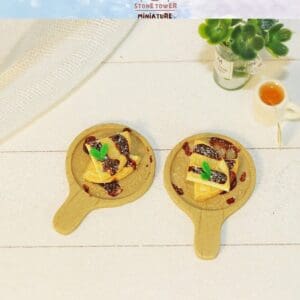 Miniature pancakes with syrup on wooden boards, beside a small plant and cup on a white surface.