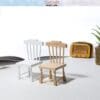 Two miniature wooden chairs, one white and one natural, on a white surface with a small radio and plant in the background.