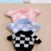 Three miniature sweaters with checkered patterns in pink, blue, and black on a textured beige background.