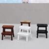 Four miniature stools in brown, white, black, and light wood on a gray background.