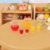 Miniature tea set and pastries on a table with pitchers of red and yellow drinks in front.