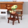 Miniature wooden stool with a clay pot of yellow flowers, set against a backdrop of wooden furniture.