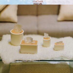 Miniature tissue boxes on a soft, textured surface in front of a blurred sofa, showcasing delicate craftsmanship.