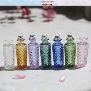Six colorful glass bottles with textured patterns and round stoppers, arranged on a marble surface with pink petals.