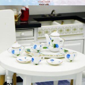 Miniature tea set with blue floral design on a round table, set in a dollhouse kitchen environment.