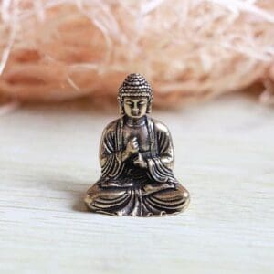 Small bronze Buddha figurine in meditation pose on a light wooden surface with a straw-like background.