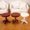 Three miniature round tables in red, brown, and white on a wooden floor, with a white sofa in the background.