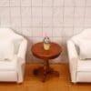 Miniature scene with two white armchairs, a wooden table, and a small drink with a pink straw against a tiled wall backdrop.