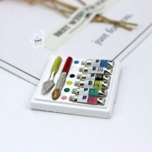Miniature paint set with tubes, brushes, and a palette on a white tray.