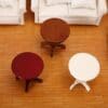 Three small round tables in varying wood finishes are arranged on a wooden floor near white sofas.