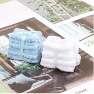 Two bundles of blue and white towels tied with ribbons on an open magazine with indoor plant images.