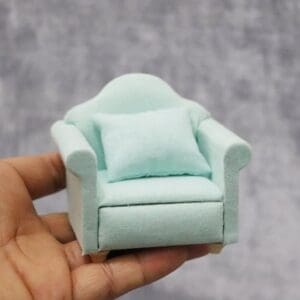 Miniature mint green armchair with a cushion, held in a hand against a gray background.