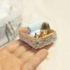 Hand holding a small decorative basket with towels, a golden faucet, and a lace trim.