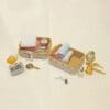 Miniature vanity set with towels, baskets, mirror, comb, and assorted toiletries on a beige surface.
