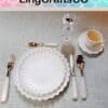 Elegant table setting with white scalloped plates, cutlery, wine glass, and teacup on a gray mat.