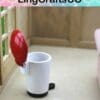 Miniature white toilet with a red lid, set in a dollhouse bathroom scene.