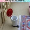 Miniature white trash can with red lid on floor near a colorful patterned rug.
