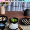A table setting with black dishes featuring various foods, chopsticks, a teapot, and decor including a sunflower.