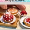 Miniature fruit tarts and desserts on white plates with a hand adjusting them, showcasing intricate edible details.