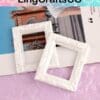 Two ornate white mini frames on a magazine and a pink textured surface.