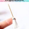 Tiny white tassel broom held between fingers with logo "LingCraftsCO" above, against a subtle colorful background.