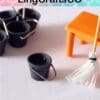 Miniature black buckets, orange stool, and mop on white surface, showcasing dollhouse cleaning tools.