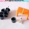 Miniature cleaning set with five black buckets, an orange table, and a small mop on a white surface.