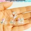 Hand holding four tiny transparent cups with floral designs.